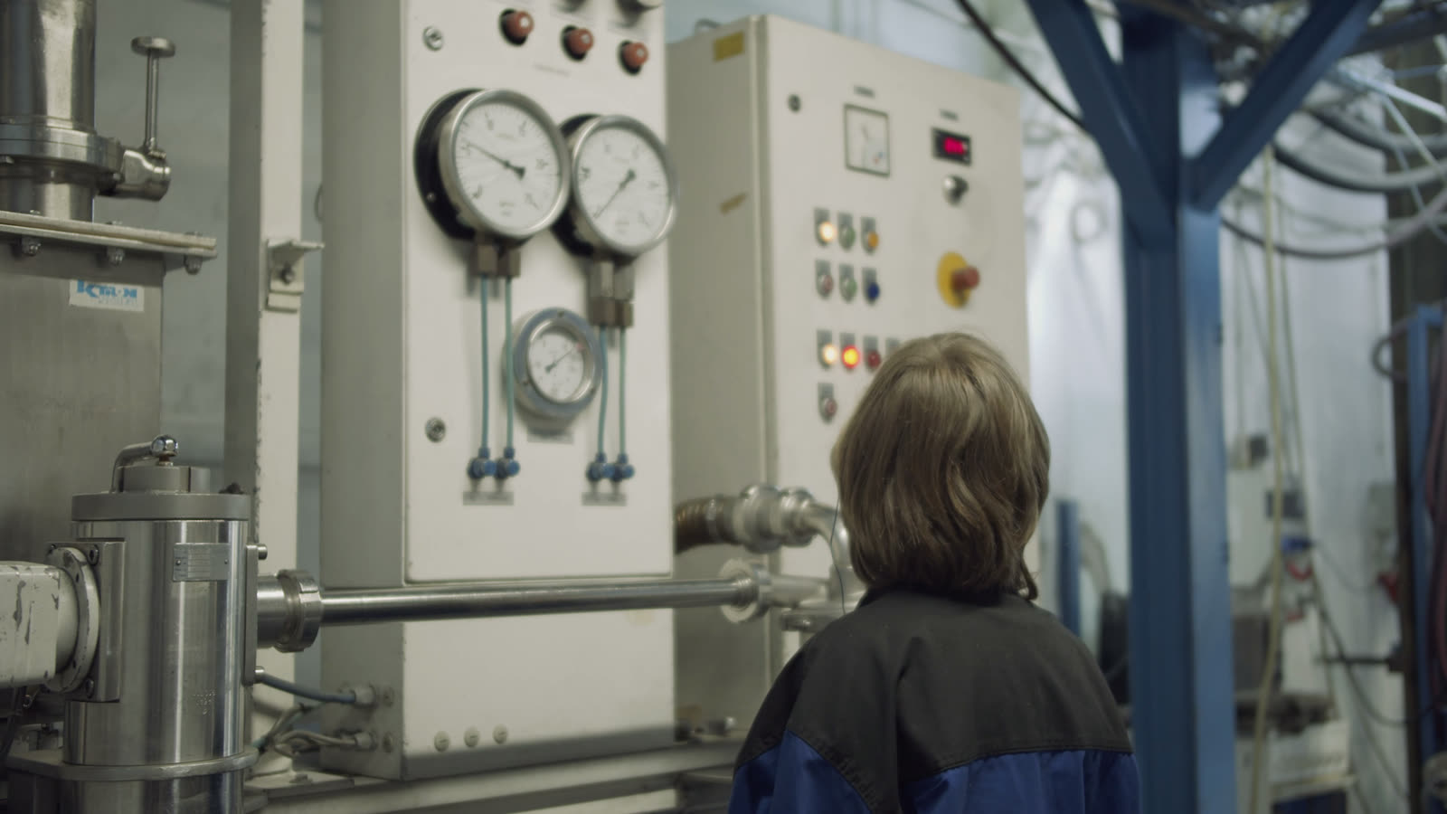 Person seen from behind in front of a wall of pipes and pressure gauges